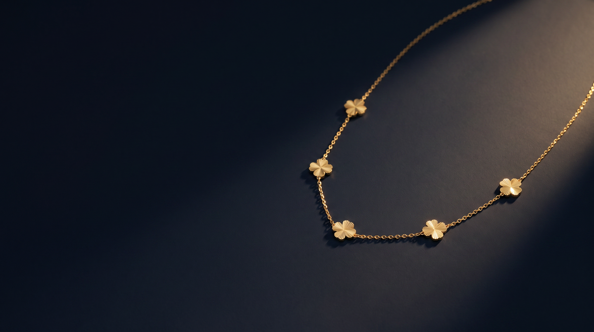 Collier trèfles en chaîne fine dorée, posé à plat sur une surface d'encre