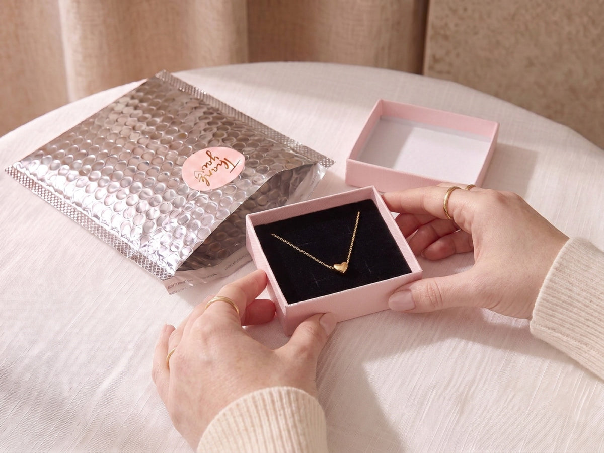 Collier cœur doré posé sur le velours noir de son écrin rose Maison Fermoir, devant son enveloppe argentée